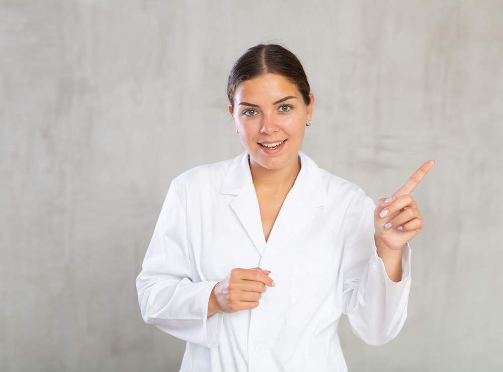 Happy young female doctor pointing to side with her finger