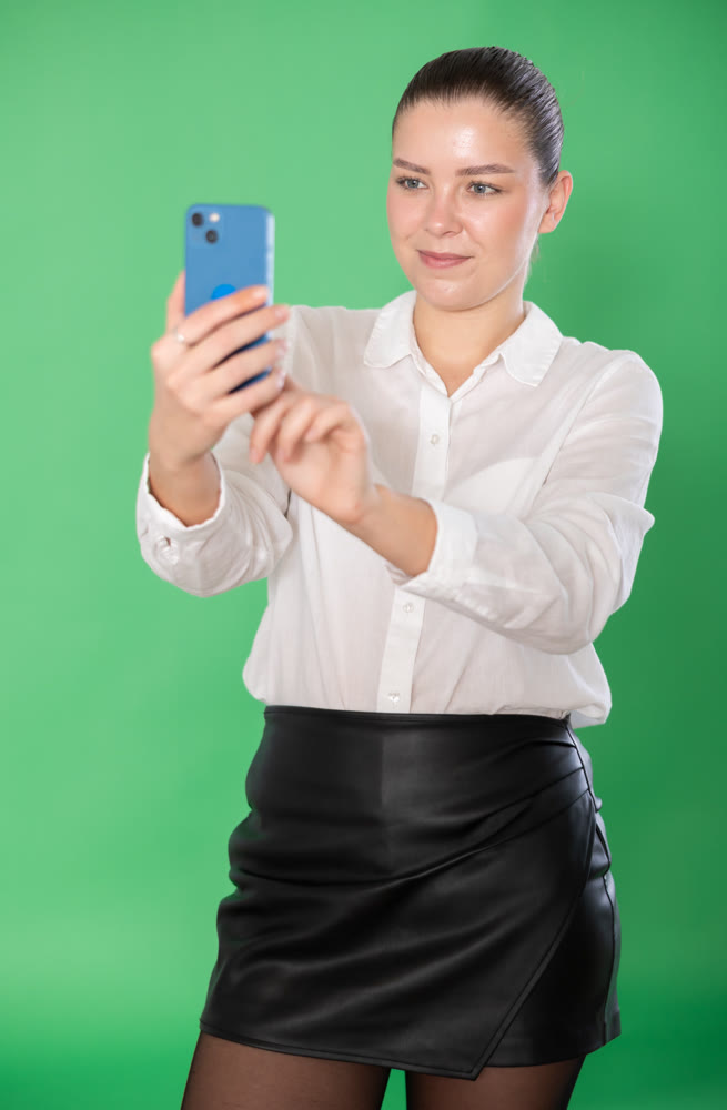 Young woman on green screen background take photo by phone camera