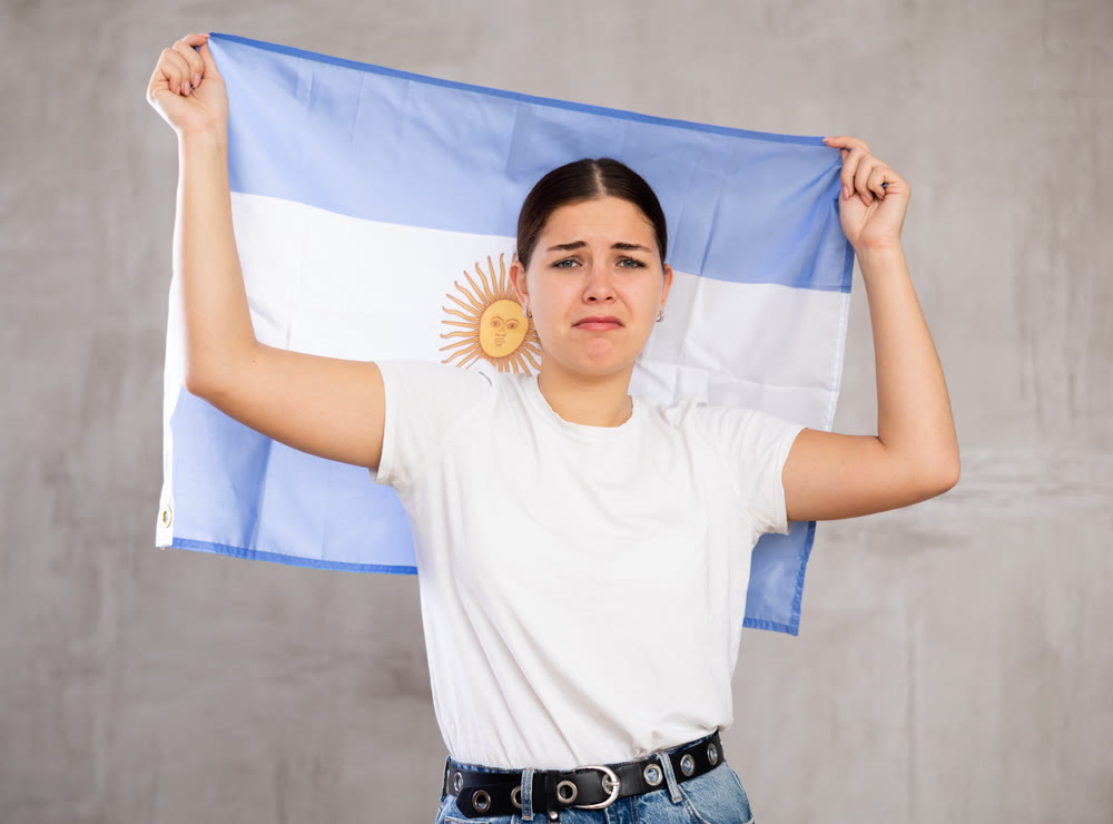 Frustrated girl with Argentinean flag behind her shoulders. Isolated on gray background