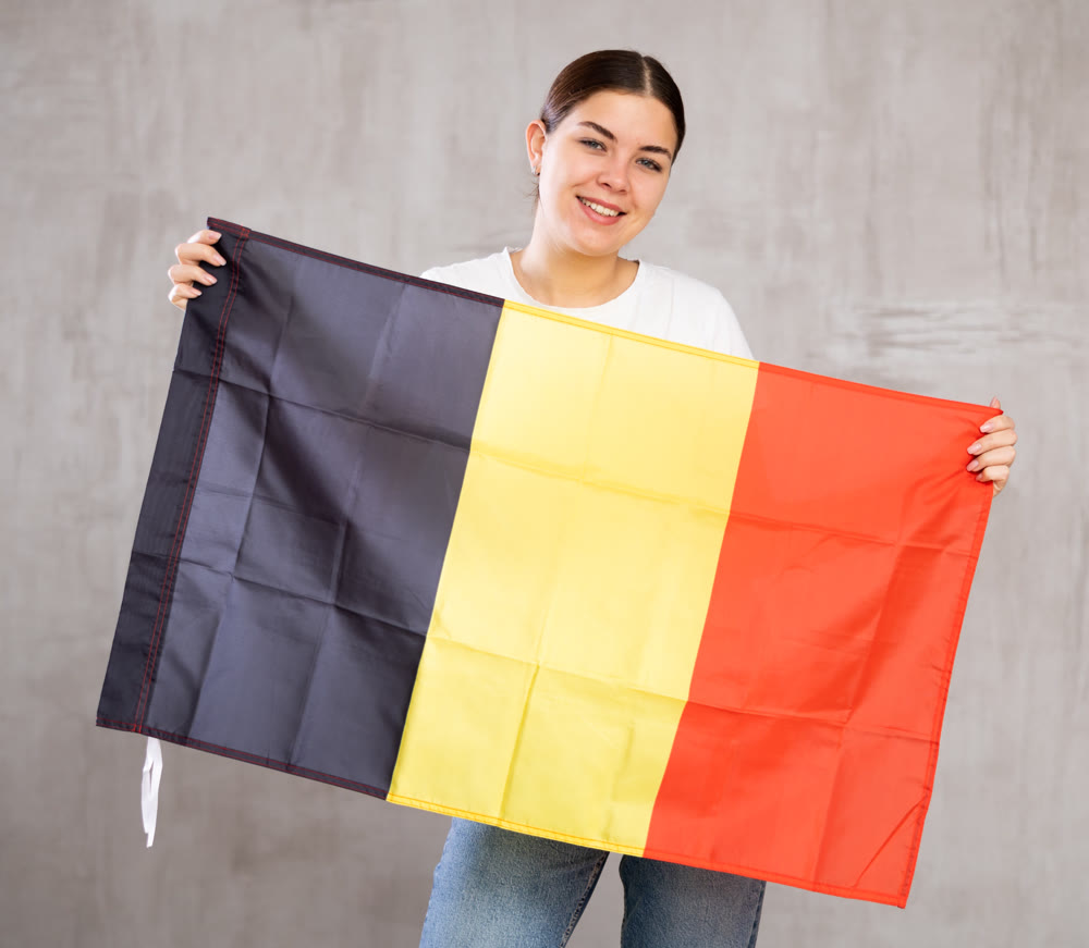Calm girl stands with flag of Belgium .Isolated on gray background