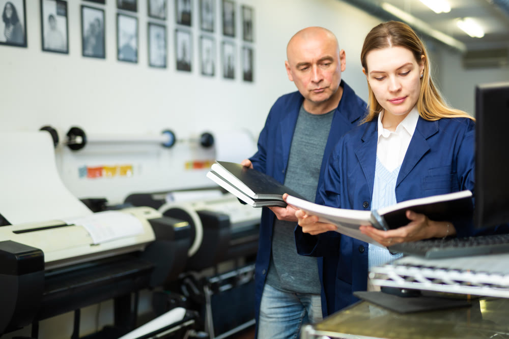 Portrait of positive female employee of a printing house with notebooks and projects in hands