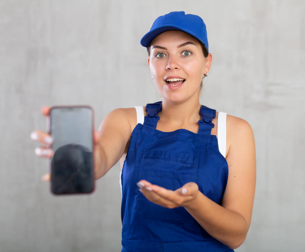 Young woman in work overalls posing with phone