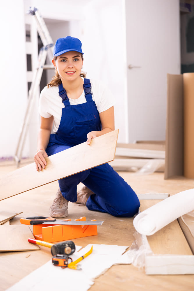 Woman builder puts laminate on the floor in room