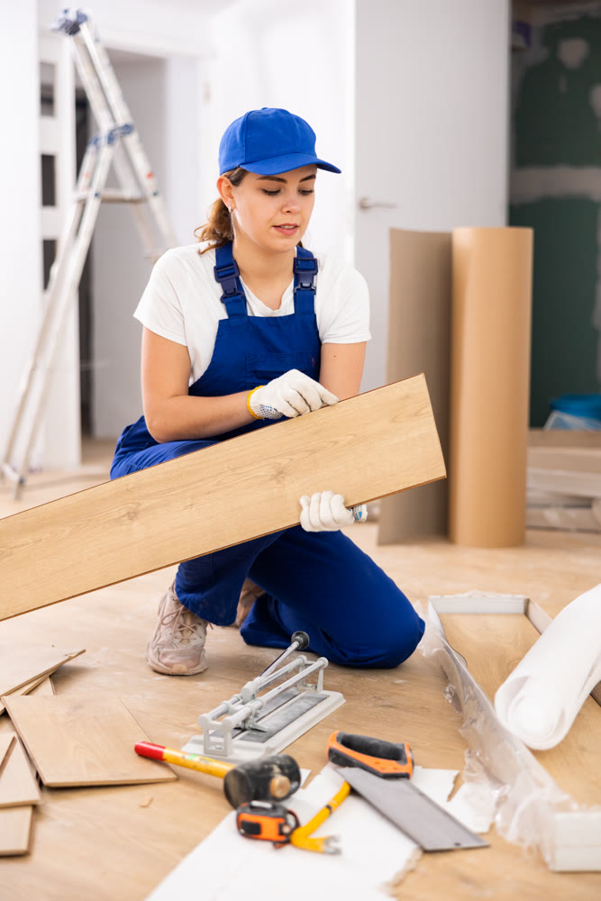 Repair in the room - woman puts laminate on the floor and checks horizontal level
