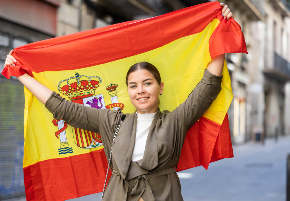 Happy young woman waving the flag of Spain on city street