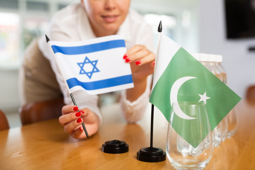 Young woman putting flags of Israel and Pakistan on table in office