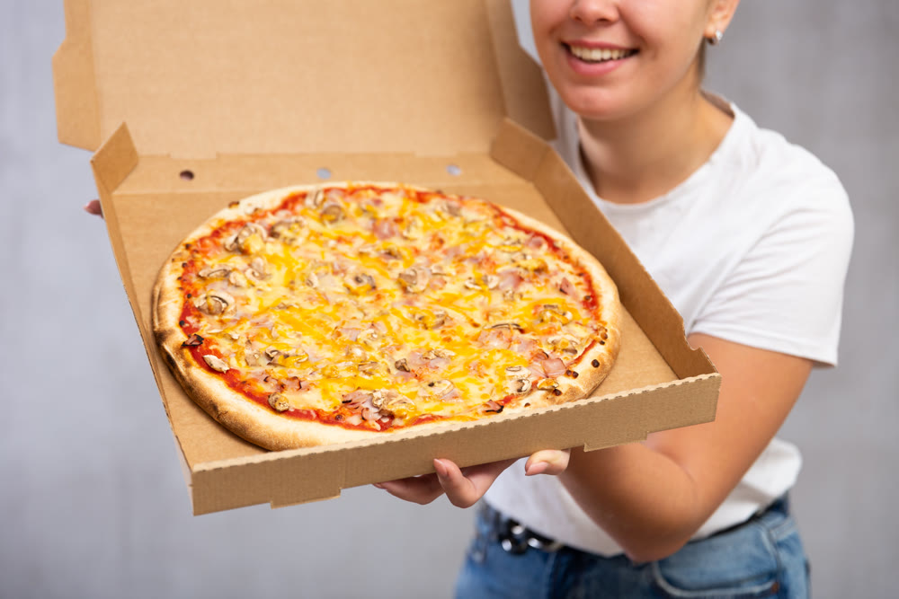 Photo of pizza held by smiling young woman against gray background