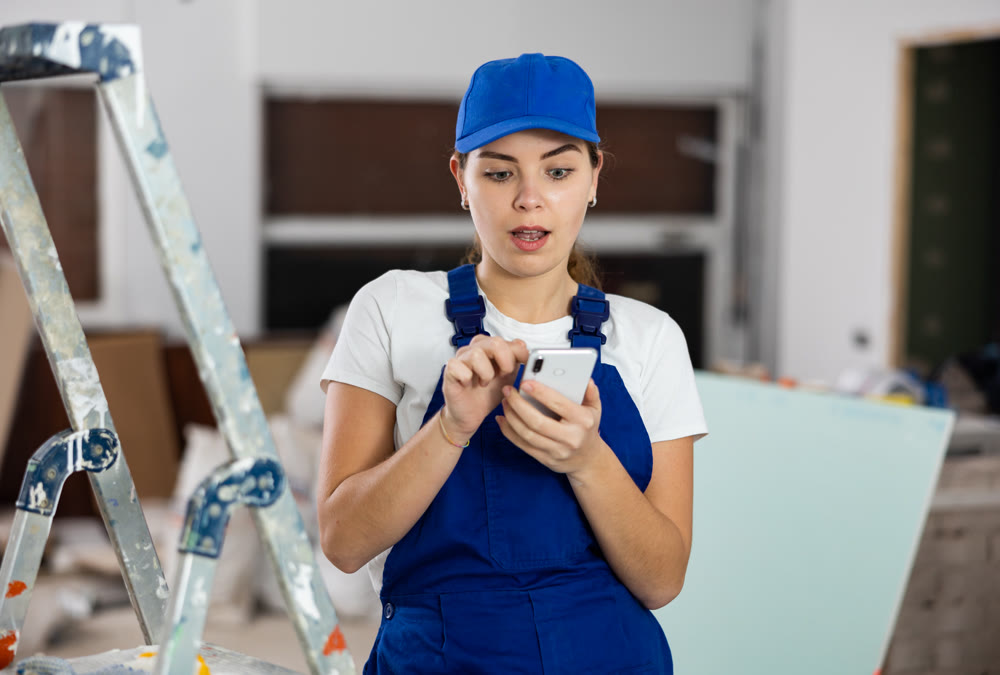 Woman builder writes a message or makes an order for building materials on phone