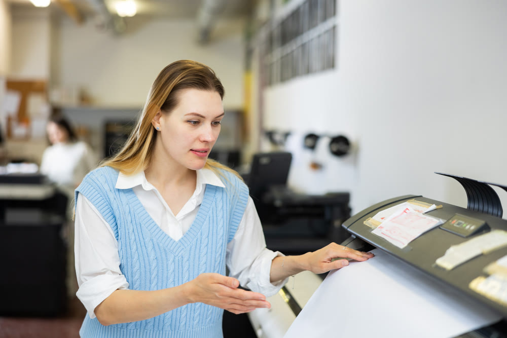 Woman employee of printing house works on modern printer