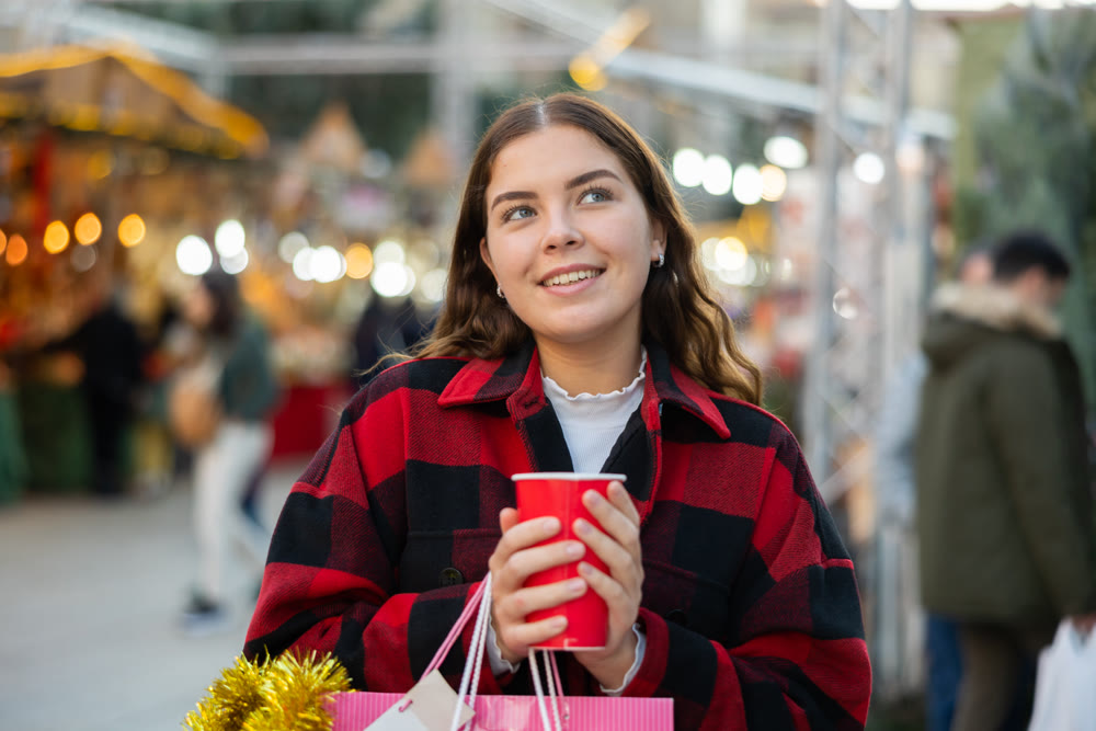 Happy girl with paper cup of coffee walking in Christmas fair