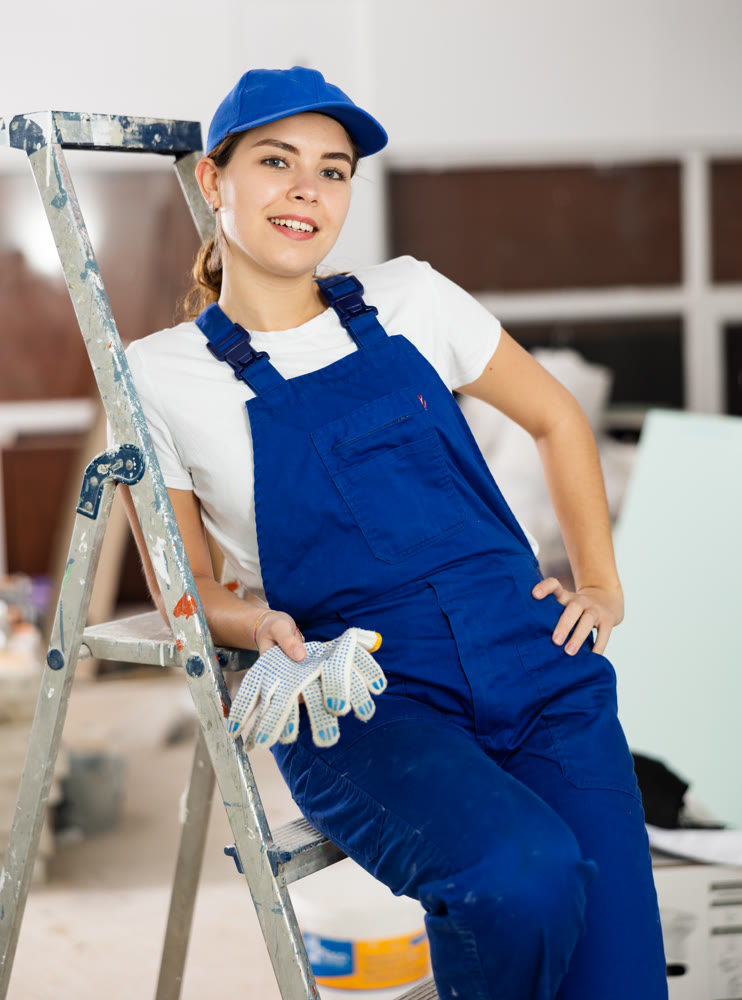 Smiling young female builder in blue uniform at construction site