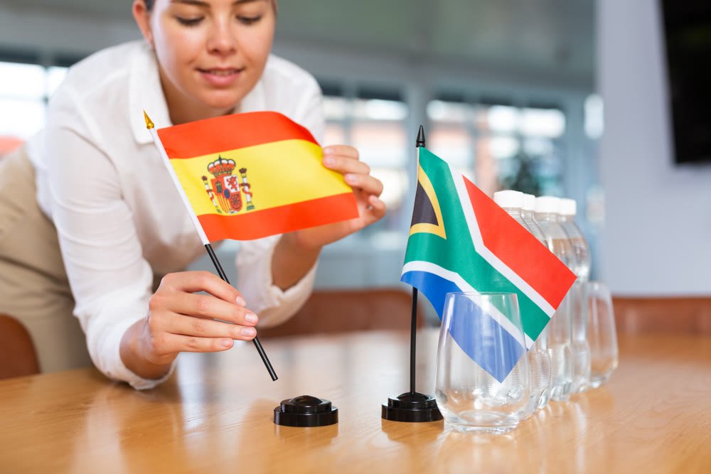 Female employee of the delegation sets flags of countries of Spain and South Africa on table before the start of negotiations