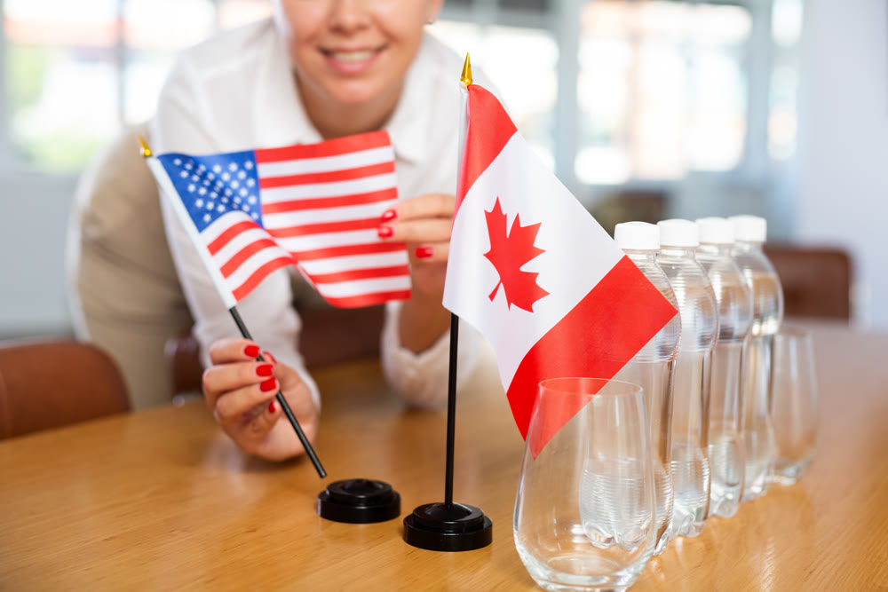 Young woman puts flags of USA and Canada on table in office