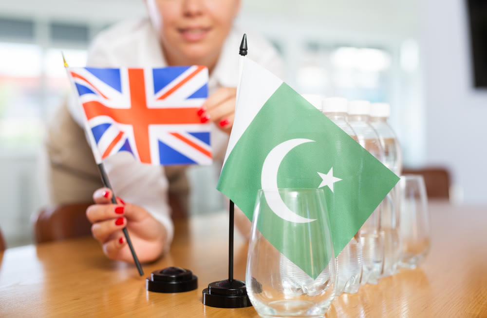 Young woman puts UK and Pakistan flags on table in office