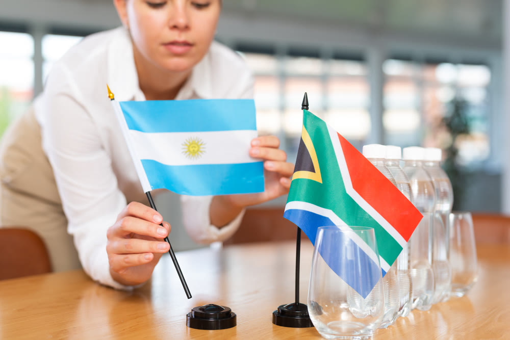 Little flag of South Africa on table and flag of Argentina put next to it by young woman