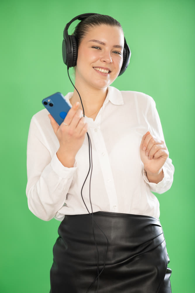 Girl wearing headphones with mobile phone in her hands enjoys music on green background