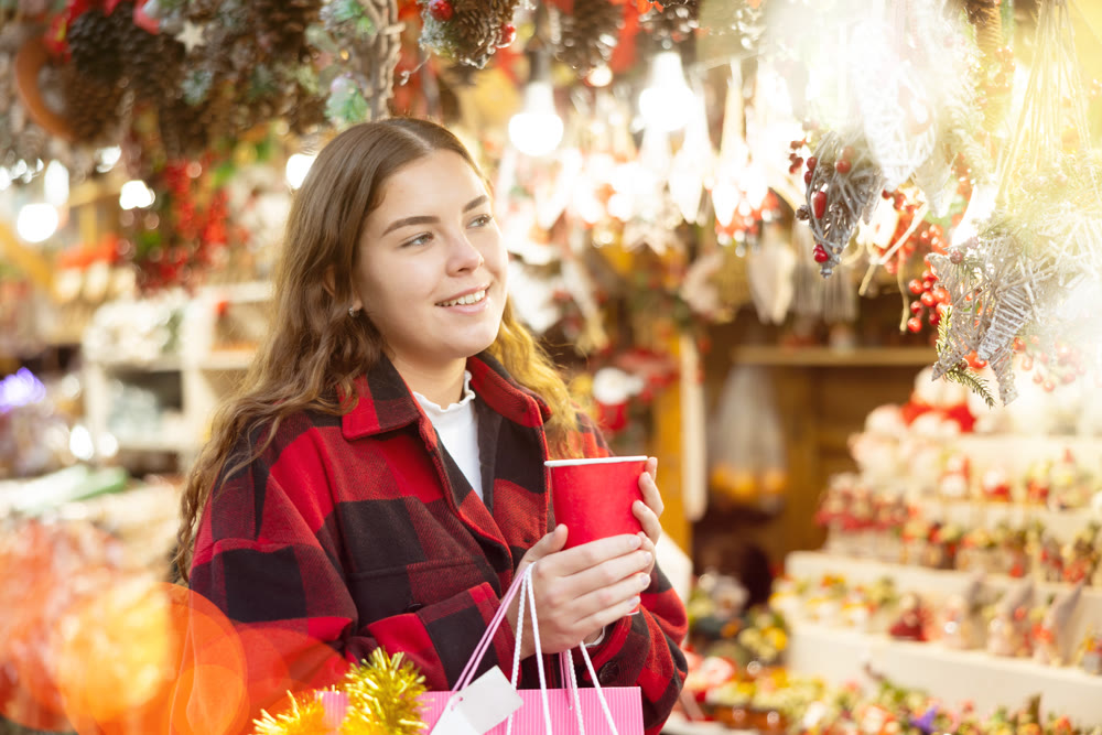 Girl with paper cup of warm drink walking at Christmas market