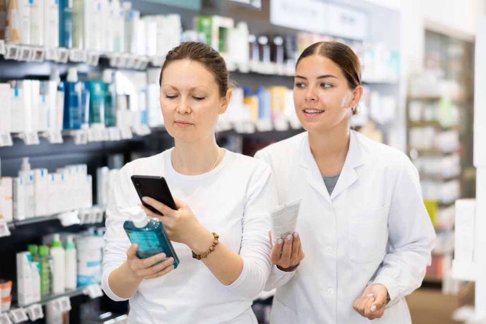 Young woman scans QR code on gel pack while friendly salesperson offers hand cream
