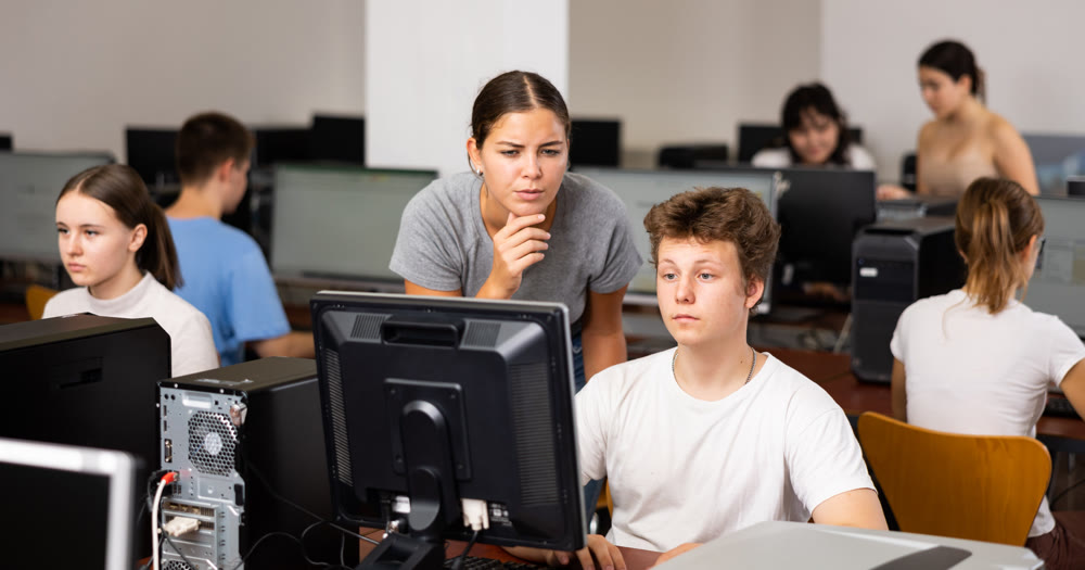 Young female teacher working with schoolboy in computer class of library