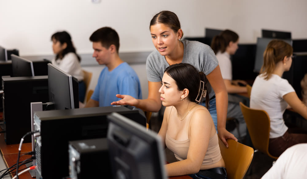 Schoolgirl using computer and teacher helping to him in class room