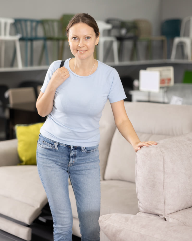 Cheerful young woman choosing new sofa in furniture salon