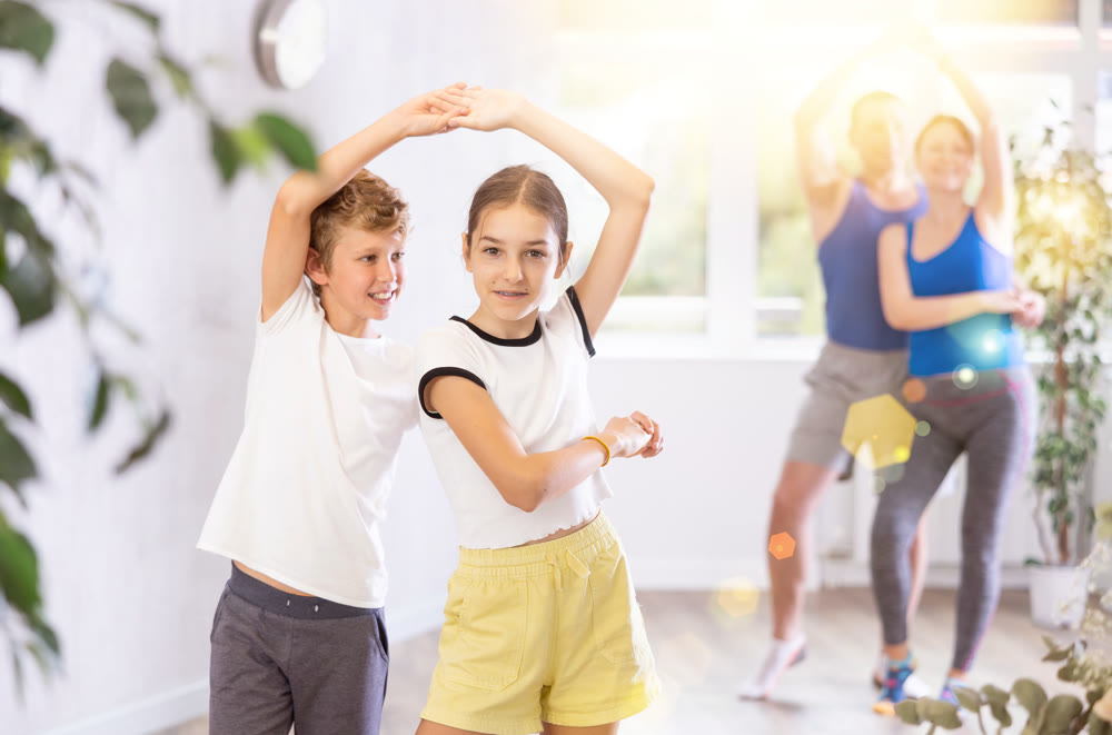 Happy preteen boy and girl practicing dance in pairs together with their parents