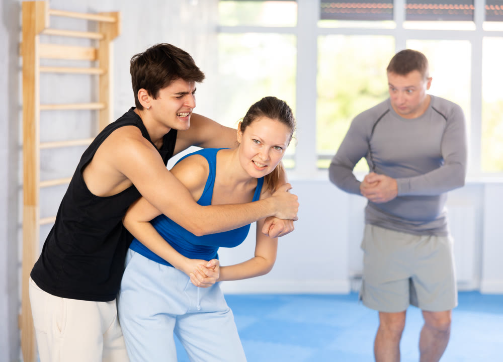 Self-defense class - a woman learns to fight back an attacking man under the guidance of trainer