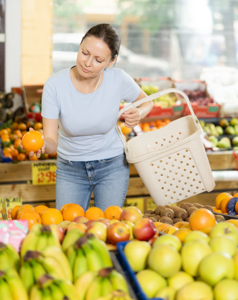 Delighted woman purchaser choosing oranges at the counter in grocery store