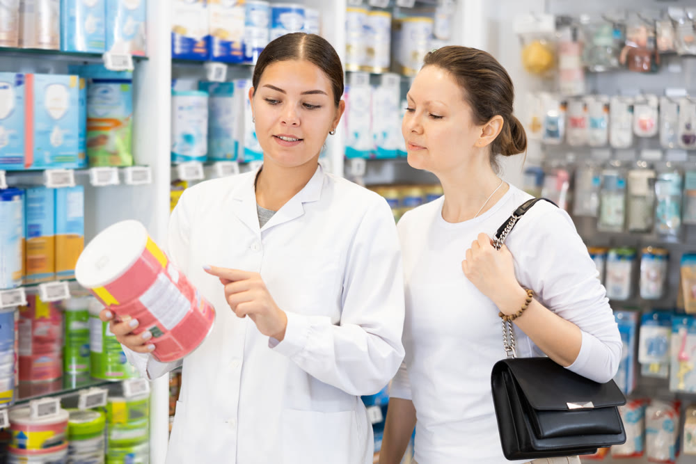 Woman pharmacist helping woman customer choose baby formula in pharmacy