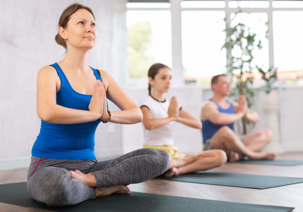 Happy middle-aged woman practicing half lotus pose of yoga with her family