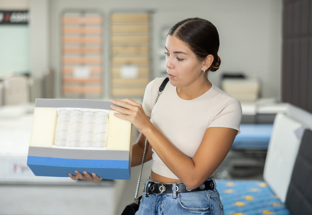 Interested young girl examining mattress cross-section sample in furniture store