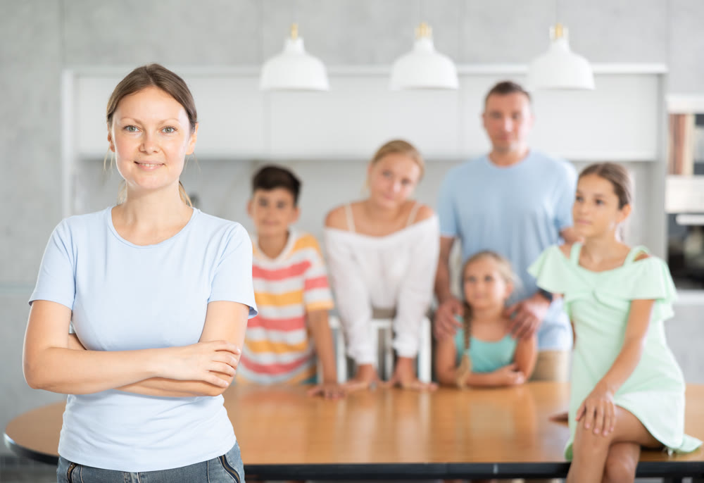 Smiling mum poses in cozy kitchen, large family with four children and husband are standing behind