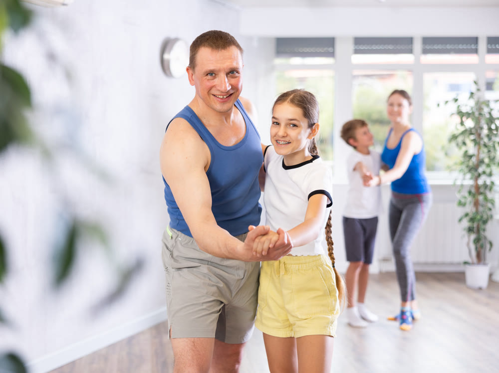 Happy father and daughter practicing dance in pairs together with other family members