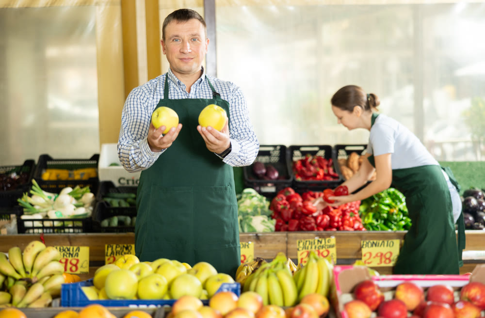 Male seller of vegetable department of store replenishing showcase with apple, put ones on showcase