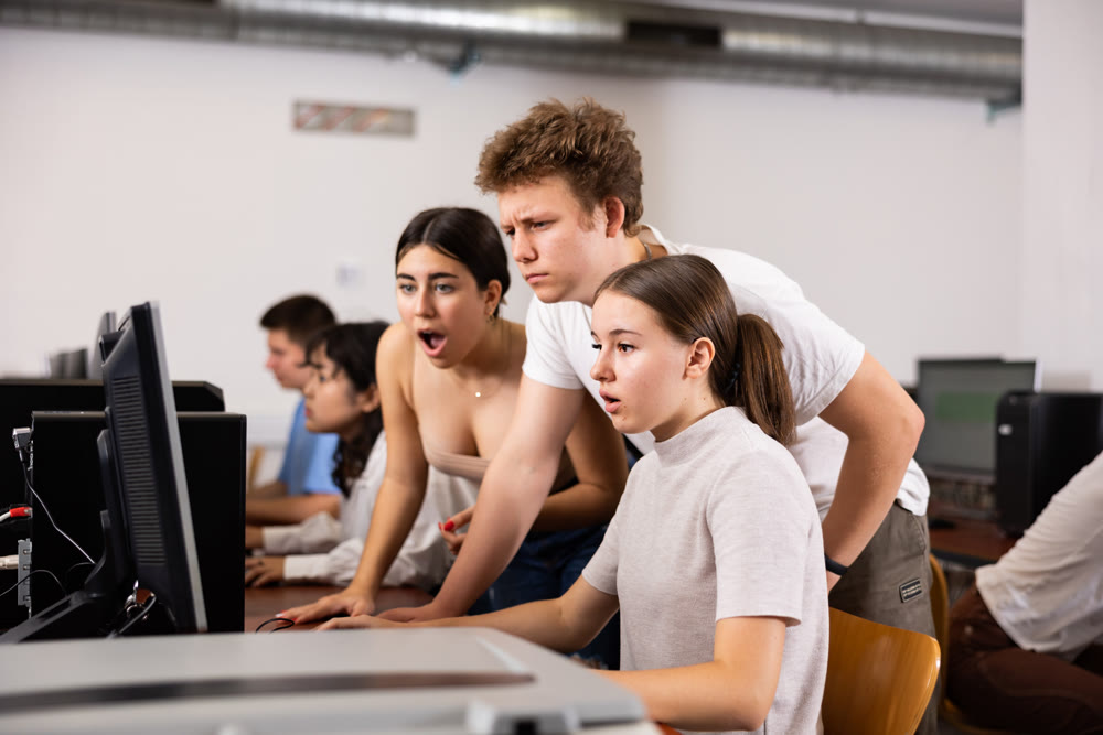 Smart teenagers giving a clue to the focused female co-learner while she is using PC in the computer classroom