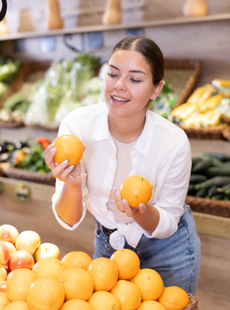 Happy smiling woman making purchases in supermarket, choosing fresh oranges
