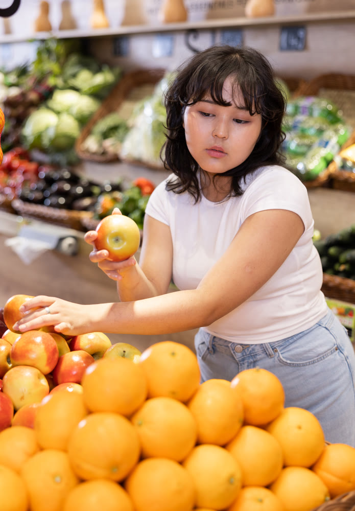 Attentive young woman purchaser choosing apples in grocery store