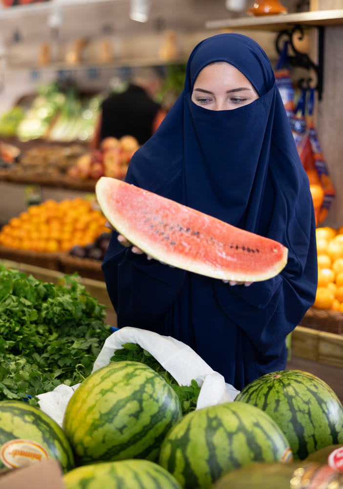 Young Muslim woman in niqab choosing watermelon in store