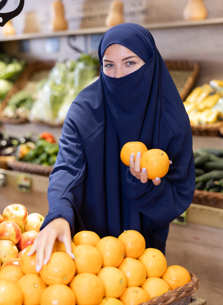 Young Muslim woman in niqab choosing oranges in supermarket