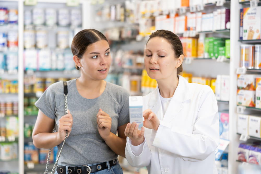 In cosmetic department of pharmacy, surprised woman listens to pharmacists story about new cream