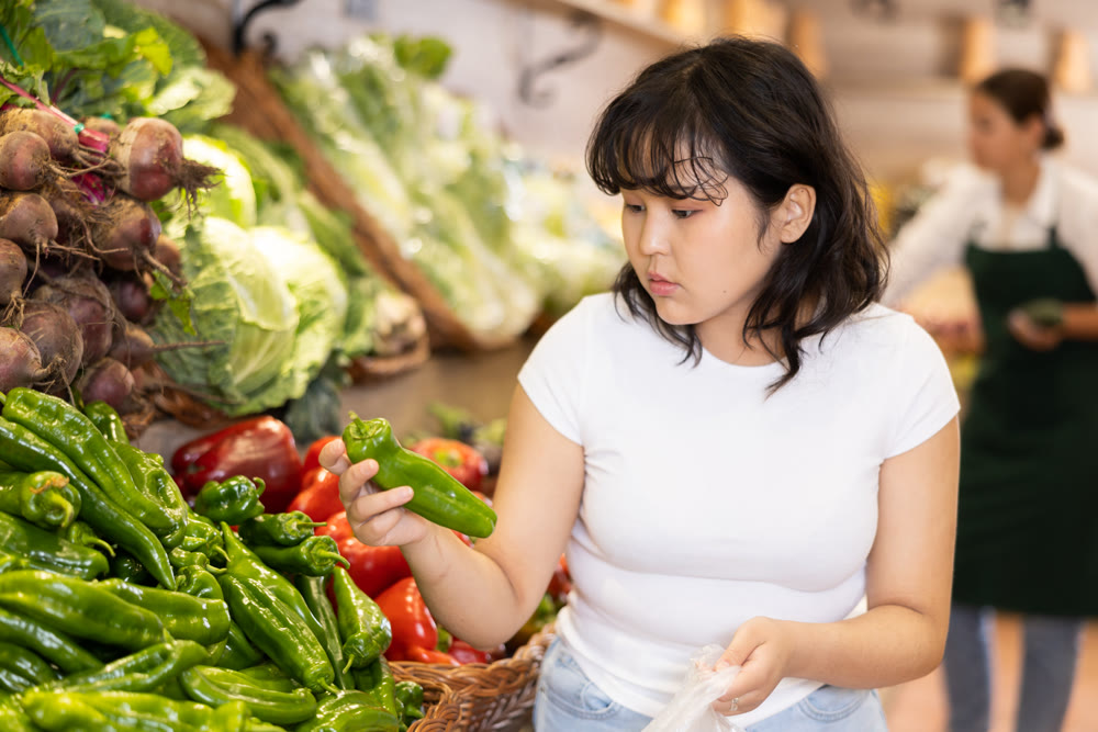 Attentive young woman purchaser choosing peppers in grocery store