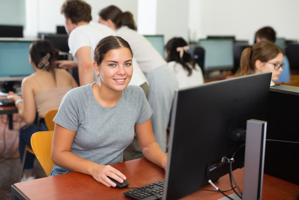 Portrait of smiling girl student looking at camera during lesson in computer class