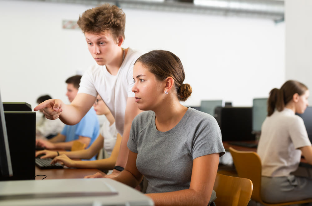 Schoolboy using computer and teacher helping to him in class room