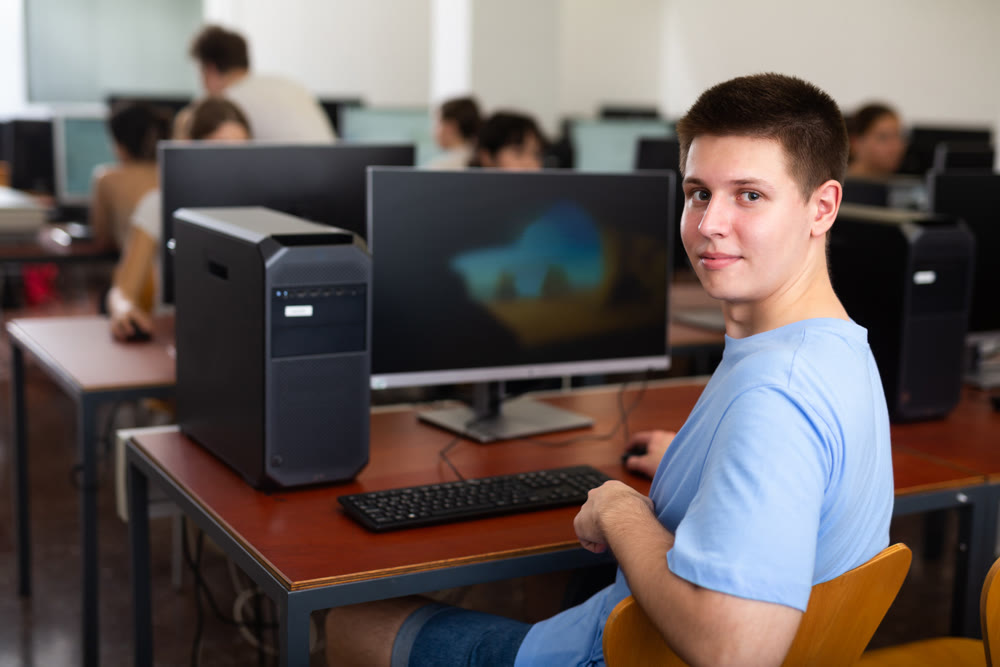 Cheerful teenager boy using PC during computer science lesson