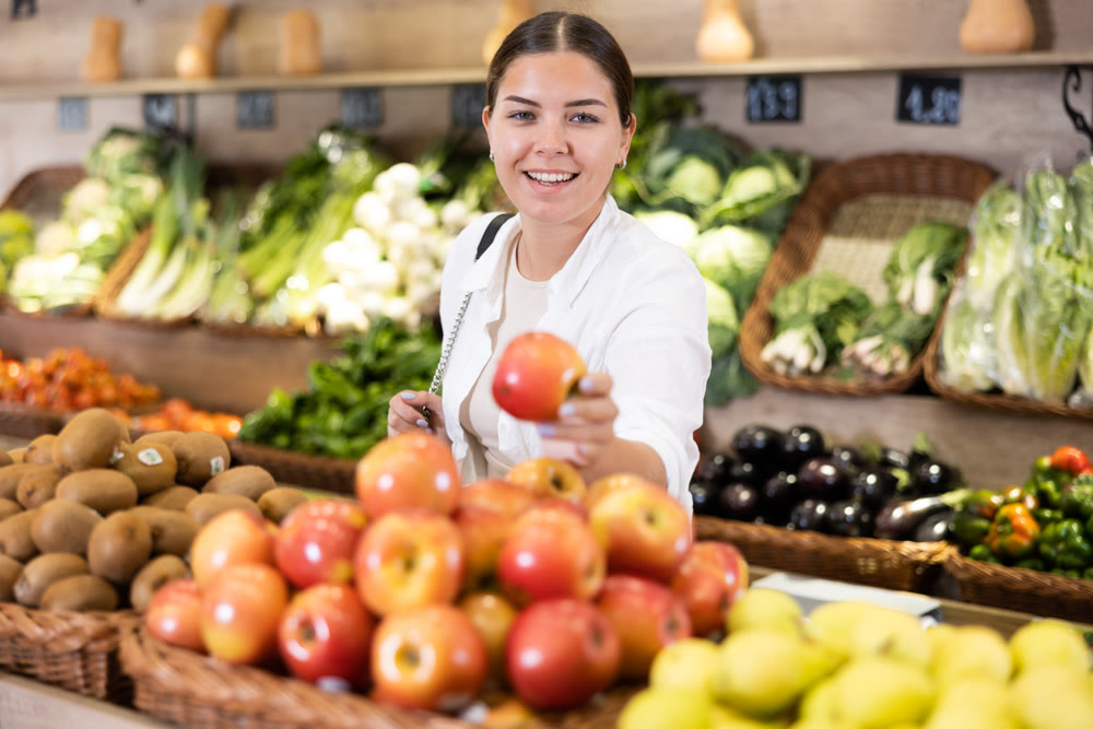 Delighted young woman purchaser choosing apples in grocery store