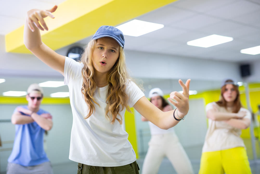 Teenage girl in cap training breakdance Toprock moves in dance hall