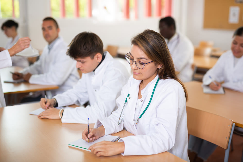 Young hispanic female medical student taking notes during group lecture