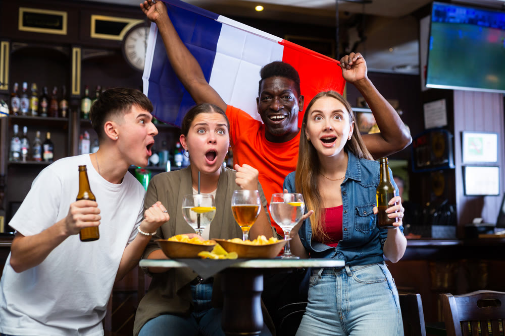 Joyful friends with France flag celebrating victory of favorite team in bar