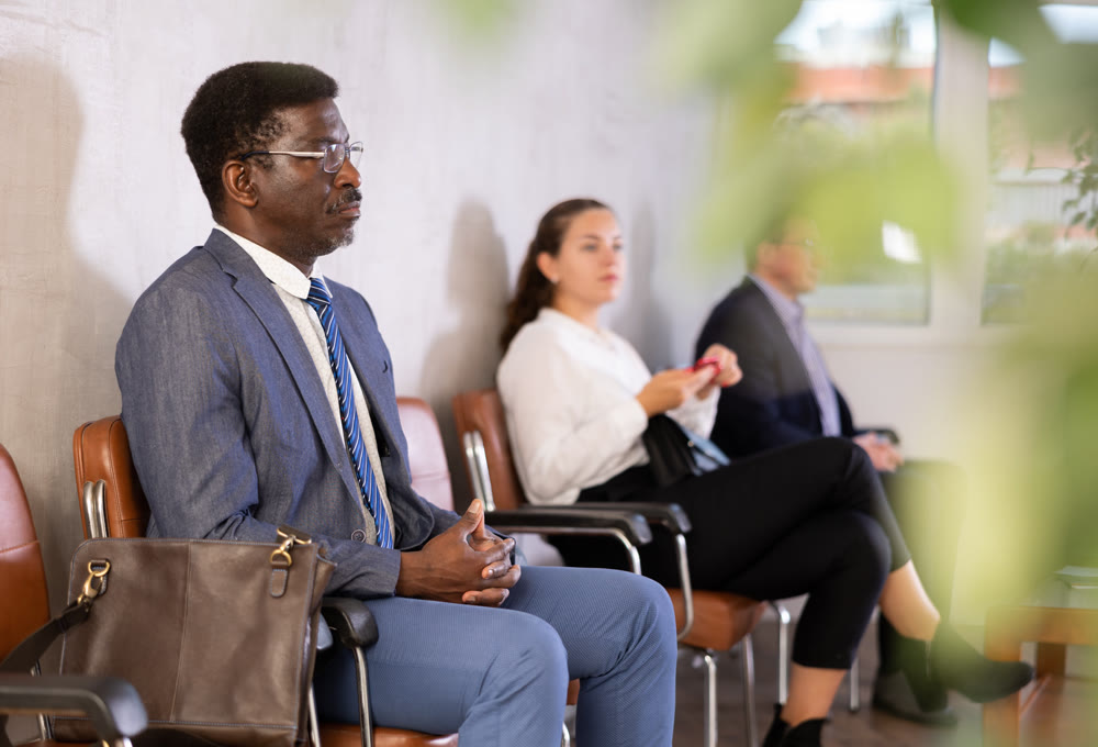 Serious-minded African male candidate siting on chair and waiting for job interview in hallway
