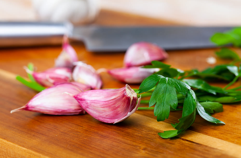 Cutting board with fresh seasonings on a wooden background. White garlic heads and cloves and parsley leaves